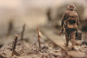 A soldier carrying a gun walks away from the camera across a muddy battelefield